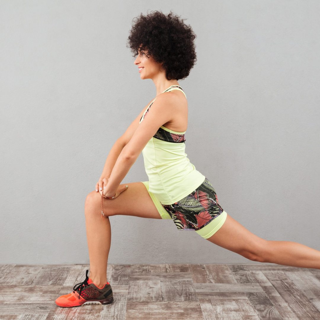 Side view of smiling curly woman stretching in studio over gray background